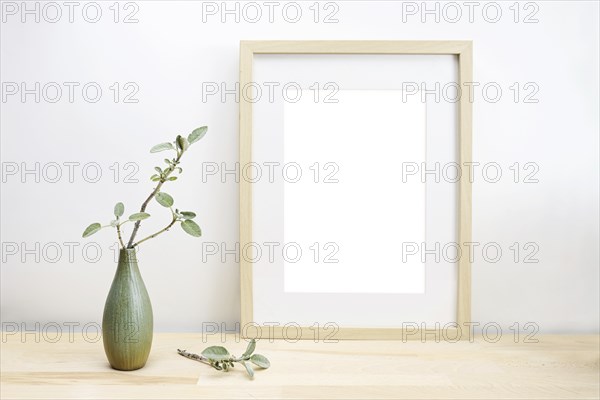 Empty wooden picture frame with passe-partout as mock-up and a vase with sage twig on a light table