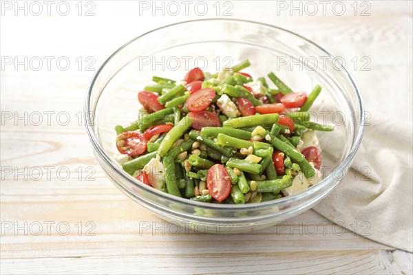 Green bean salad with tomatoes, pine nuts and feta cheese in a glass bowl on a light wooden table,