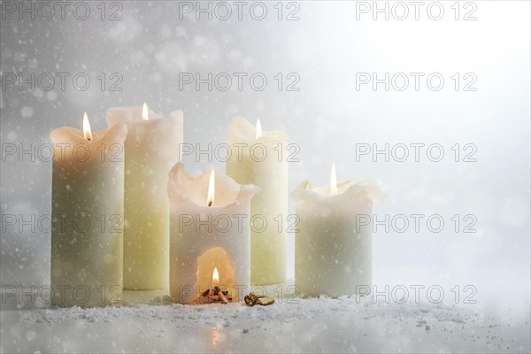 White candles burning in the snow, in one is a carve with a warm campfire, surreal winter still
