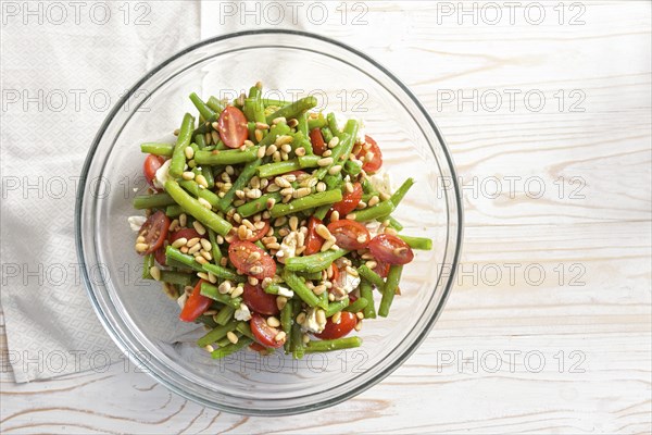 Antipasto salad of green beans, tomatoes, pine nuts and feta cheese in a glass bowl on a light