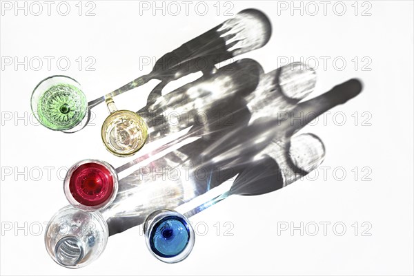 Drinking glasses with colorful liquids and a water bottle are casting shadows on a bright