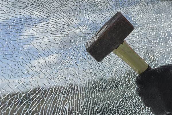 Gloved hands of a criminal destroying a laminated glass window with a hammer, violence, burglary
