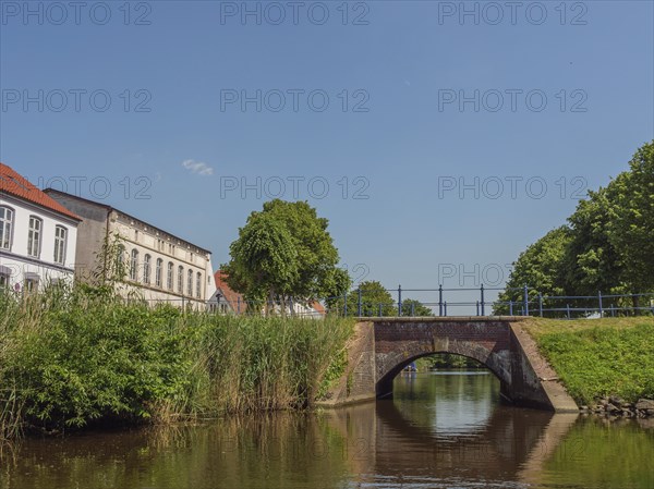 A small bridge over a river with buildings and green bushes in the background, friedrichstadt,