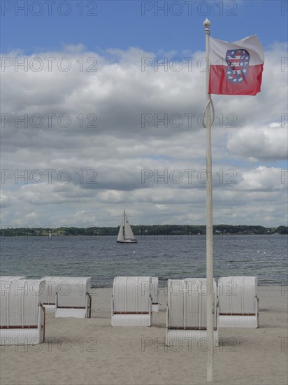 Single flag and several beach chairs on a sandy beach, sailing boat on the sea under a cloudy sky,