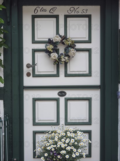 A beautifully decorated door with a wreath of flowers and a flower box underneath, Schleswig,