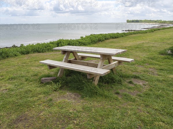 A picnic table on green grass with a view of a lake and a cloudy sky, Maasholm, Schleswig-Holstein,