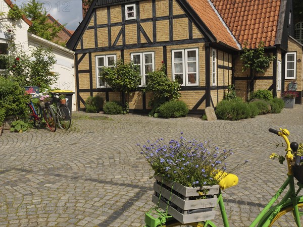 Half-timbered house with blooming flowers and a bicycle on a cobblestone street, Kappeln,
