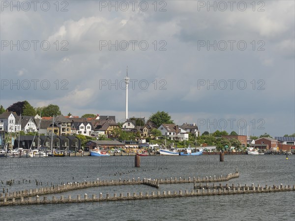 A city view with a television tower, buildings and boats on the waterfront under a partly cloudy