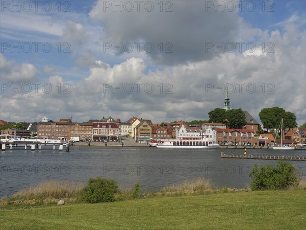 Panorama of a riverside town with historic buildings under a partly cloudy sky, Kappeln,