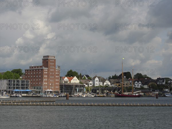 Buildings and boats along a coastline under a cloudy sky, Kappeln, Schleswig-Holstein, Germany,
