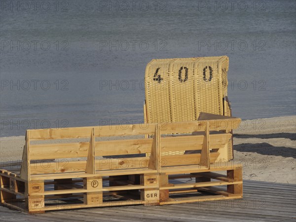 A single beach chair and a wooden bench on a quiet beach with a view of the water under a clear