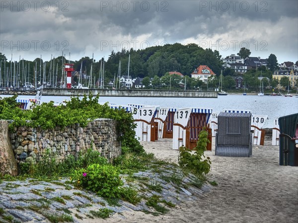 Beach with numbered beach chairs, boats in the water and a lighthouse in the background,