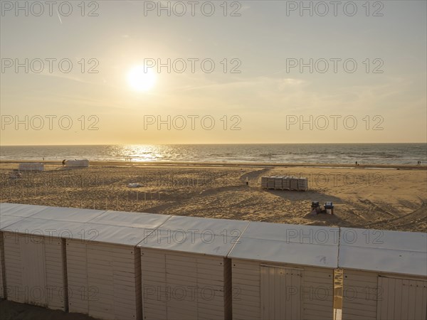 A peaceful sunset on the beach with huts in the foreground and the sea in the background, de haan,