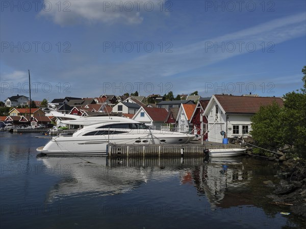White yachts in the harbour in front of houses with red roofs. Calm water reflects the boats and