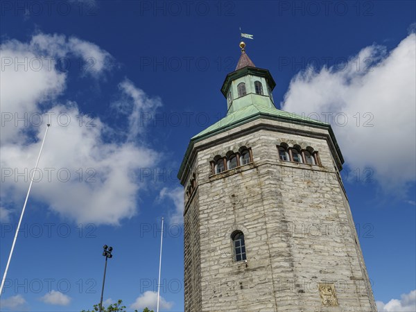 Historic stone tower with clock and flag under a bright blue sky, Stavanger, Norway, Europe