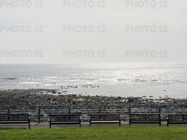 Panoramic view of the sea with benches in the foreground and shiny water surface, Newcastle,