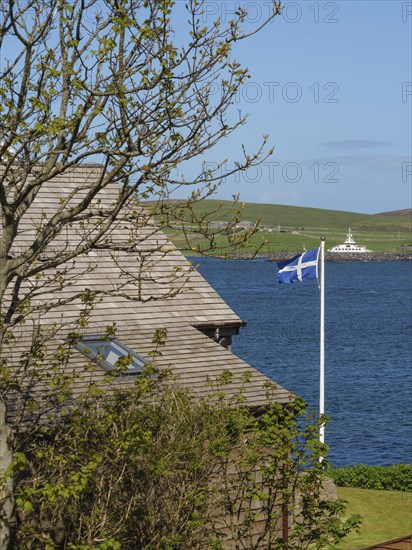 View of a coastal landscape with a house roof, a tree and a Scottish flag, Lerwick, Shetlands,
