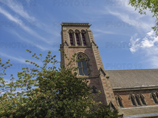A gothic church tower rises into the sky, surrounded by trees and clouds, inverness, Scotland,