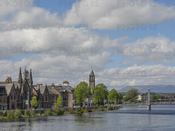 Historic buildings and a bridge over the river, surrounded by trees with mountains in the