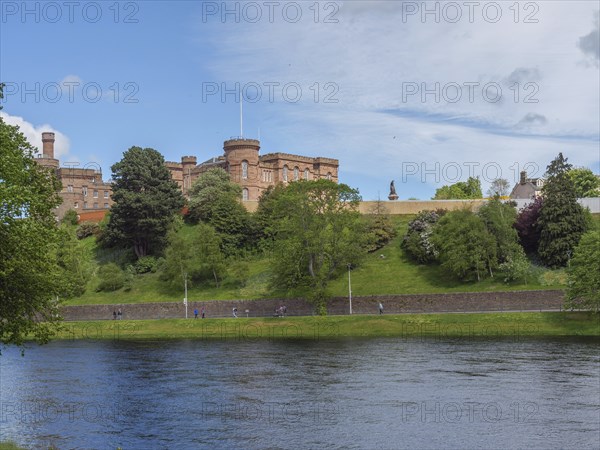 View of a castle on a hill, below a calm river with green banks and a spring-like sky, inverness,