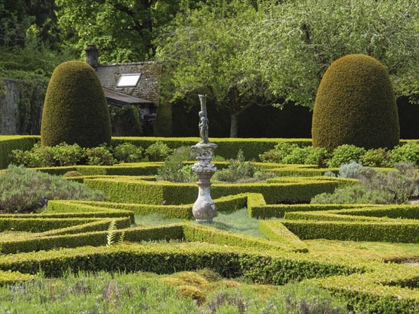 A formal garden with symmetrically trimmed hedges and a central sculpture, all set in a verdant