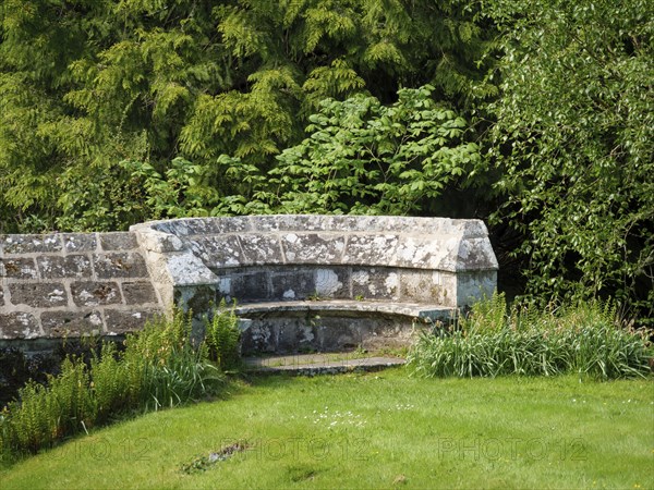 An old stone bench in a historic garden surrounded by green trees and plants, inverness, Scotland,