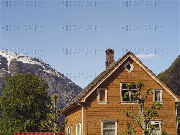 A brown wooden house with a high roof in front of a mountain panorama under a clear sky, Eidfjord