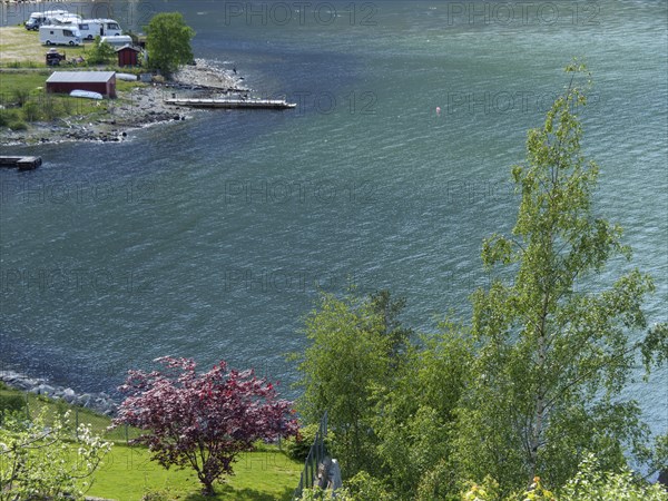 A lake with calm blue water, trees along the shore and some camping and boating facilities in the