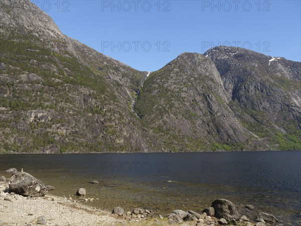A lake surrounded by high mountains with a waterfall, blue sky and green vegetation, Eidfjörd,