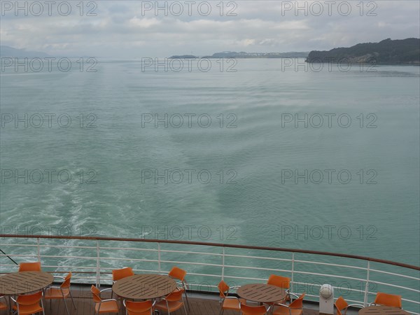 Tranquil view of the sea from the back of a ship with empty table groups and orange-coloured chairs