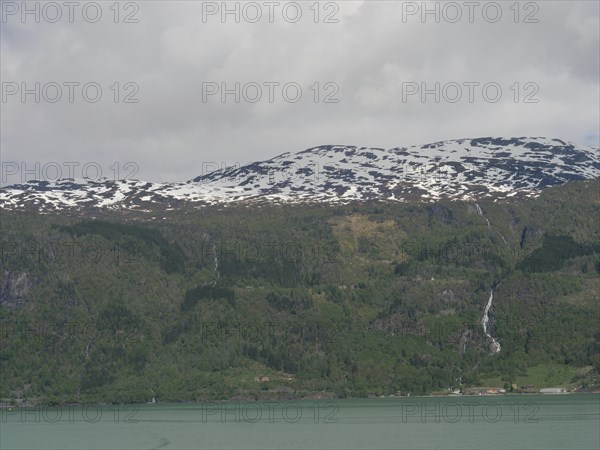 View of snow-capped mountains with waterfalls and a calm lake below, Eidfjord, Norway, Europe