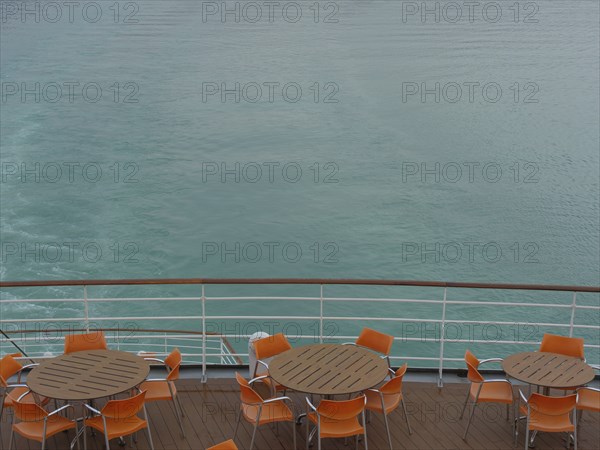 Deck of a ship with tables and chairs in orange, calm water in the background, Eidfjord, Norway,