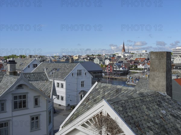 Urban scene with traditional houses, a church and water in the background under a clear blue sky,