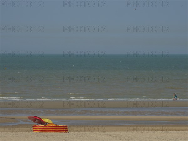 Beach with a colourful parasol and an orange and yellow striped deckchair in front of calm sea and