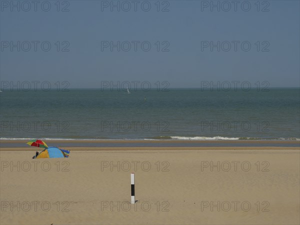 A quiet beach with a small tent in the sand, the sea in the background and a blue sky above, de