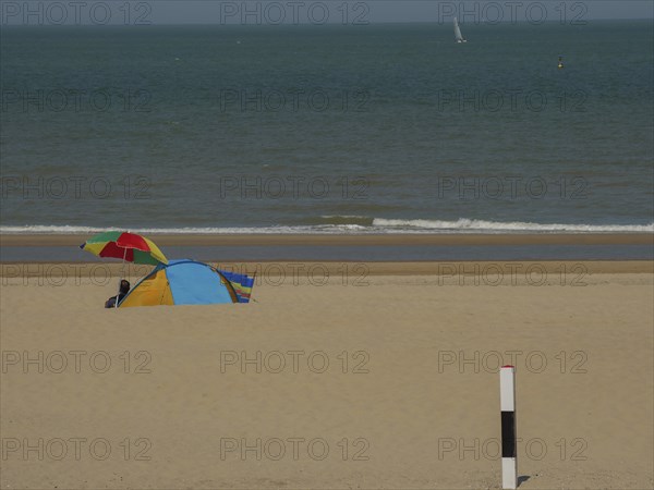 Colourful tent and parasol on a sandy beach, with calm sea in the background on a sunny day, de