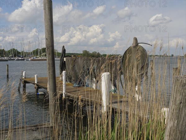An old jetty on the lake with folded fishing nets, boats and clouds in the sky in the background,