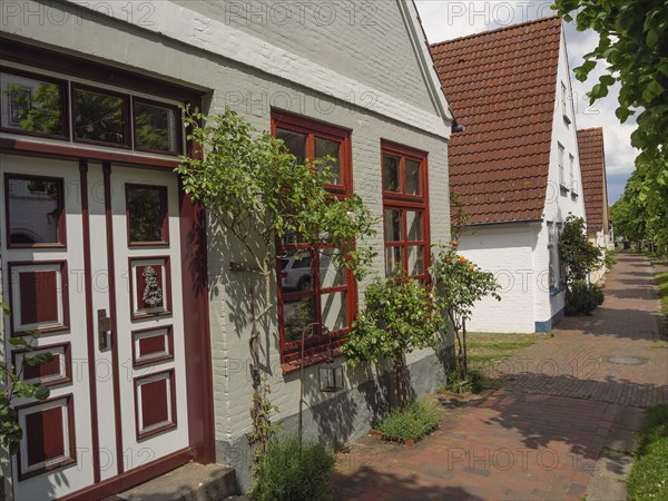 A brick-style house with red windows and a door, surrounded by plants, on a sunny day, Kappeln,