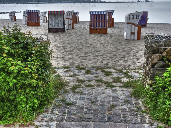Beach chairs on a sandy beach with moss-covered cobblestones, against the backdrop of a calm sea