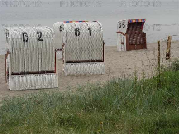 Several white beach chairs with numbers stand in front of a calm sea on a sandy beach, Eckernförde,