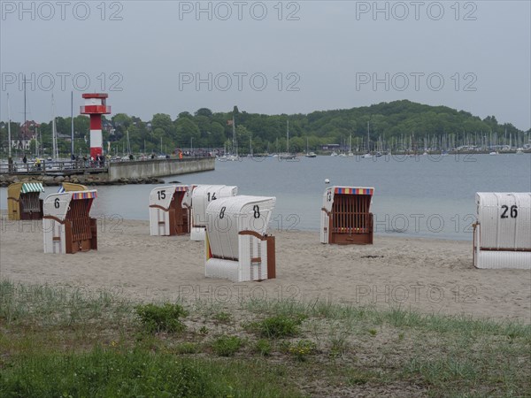 Lonely beach with numbered beach chairs and view of a lighthouse and boats in the background,