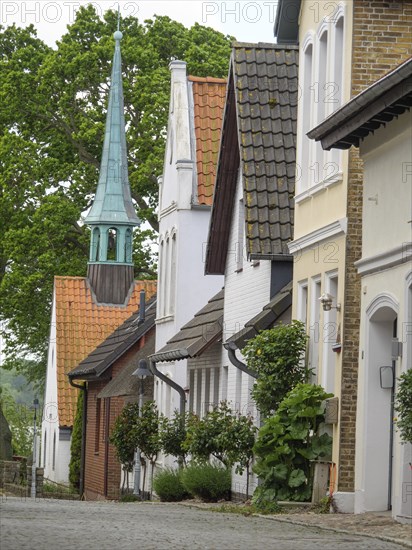 A street with historic buildings and a striking church tower, surrounded by trees and houses with