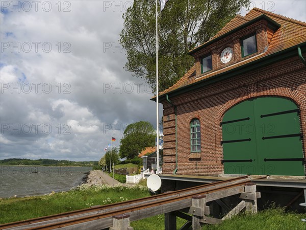 Red brick building with green Tor tor on the waterfront with railway tracks and flagpoles,