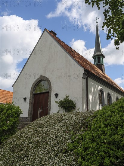 White church with high tower and red roofs, surrounded by bushes under a blue sky, Maasholm,