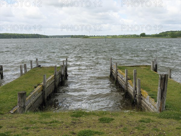 View of two harbour jetties with grass and wooden piles protruding into the water, Maasholm,