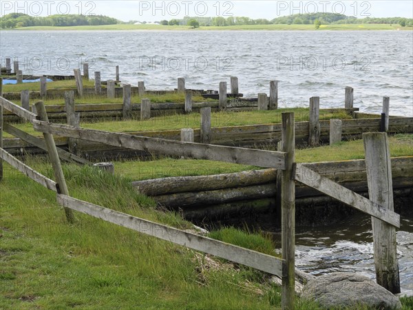 Wooden fences and green areas in a quiet harbour area with water in the background, Maasholm,