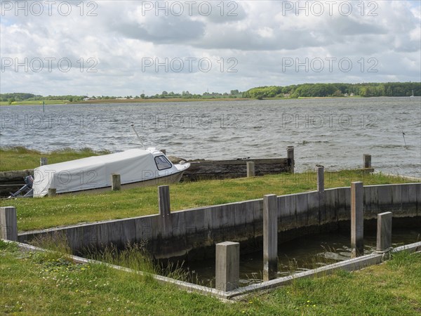 Boat in a harbour area on the water with green shore and cloudy sky, Maasholm, Schleswig-Holstein,