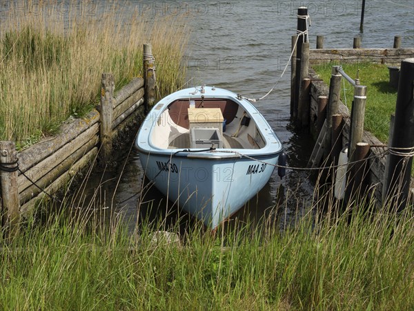 Blue boat in a narrow waterway between wooden jetties on a quiet shoreline, Maasholm,