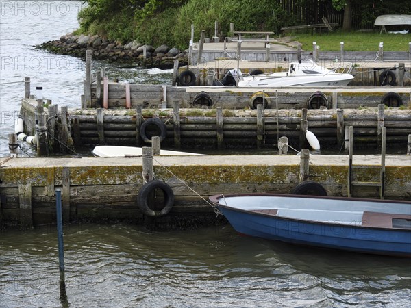 A quiet little harbour with several boats along a wooden jetty and surrounding green vegetation,