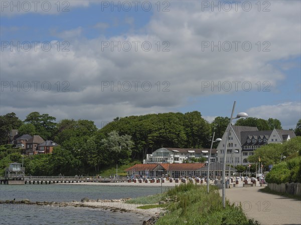 A coastal landscape with a promenade, small houses and green areas under a slightly cloudy sky,